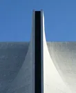 A curved concrete building facade against a blue sky, with a dark vertical seam down its centre.